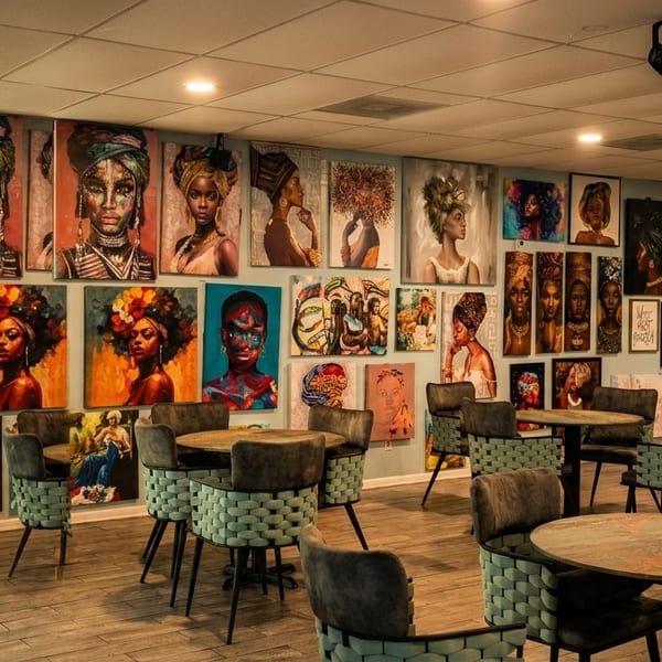 Restaurant dining room with numerous vibrant portraits of Black women on the walls and round tables with chairs.