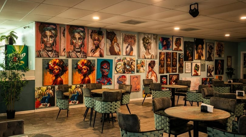 Restaurant interior with numerous vibrant portraits of Black women on the walls and round tables with chairs.