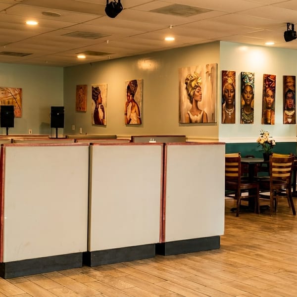 Restaurant interior with green booths, wooden tables, and walls adorned with diverse art pieces.