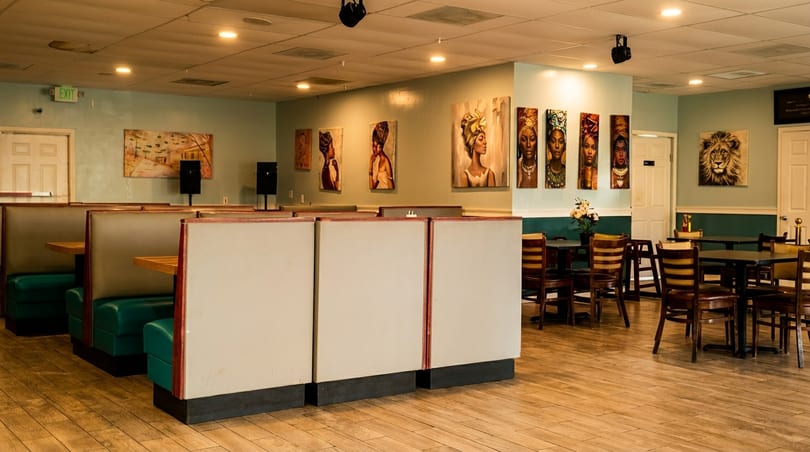 Restaurant interior with booths, tables, chairs, and diverse artwork on light blue walls.