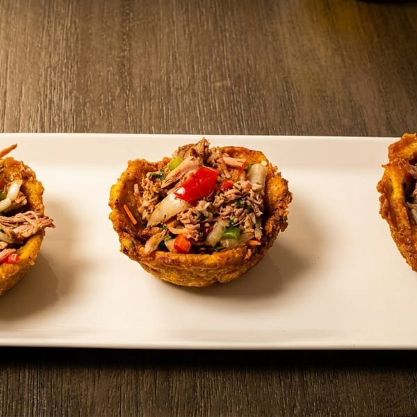 Three golden plantain cups filled with shredded meat, red and green peppers, and onions.