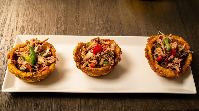 Three golden plantain cups filled with shredded meat, red and green peppers, and onions.