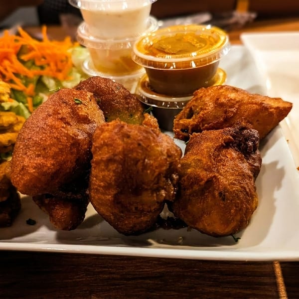A platter of fried fish, plantains, fritters, salad, and dipping sauces on a wooden table.