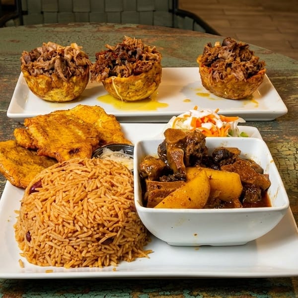 Two plates of Caribbean food on a rustic table, featuring mofongo, rice, plantains, and stew.