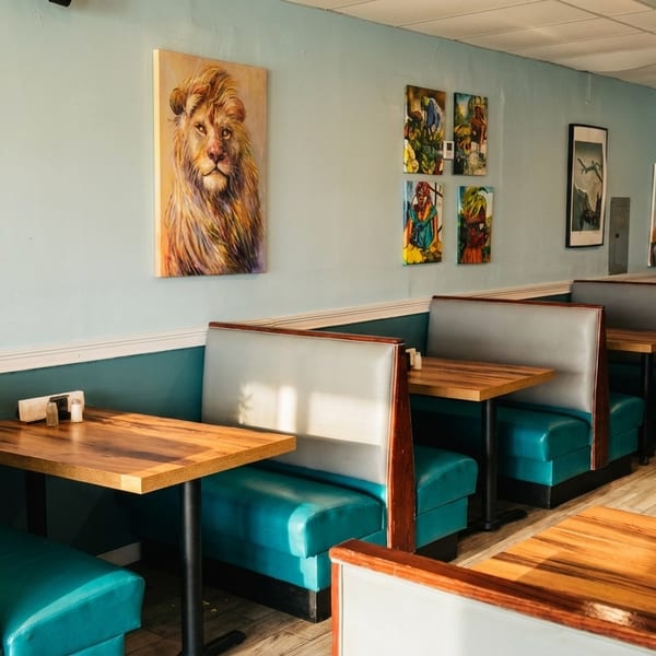 Restaurant interior with teal booths, light blue walls, wooden tables, and vibrant African-inspired artwork.