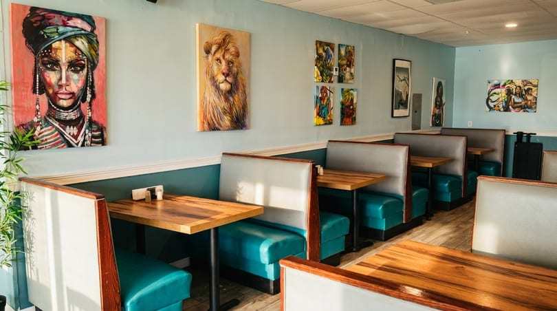Restaurant interior with teal booths, light blue walls, and diverse artwork, including a large portrait.