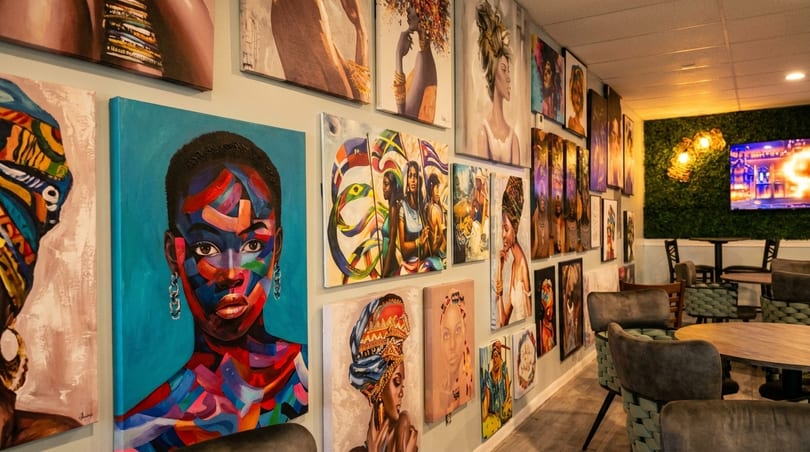 A restaurant interior with a wall full of vibrant, colorful paintings and a seating area.