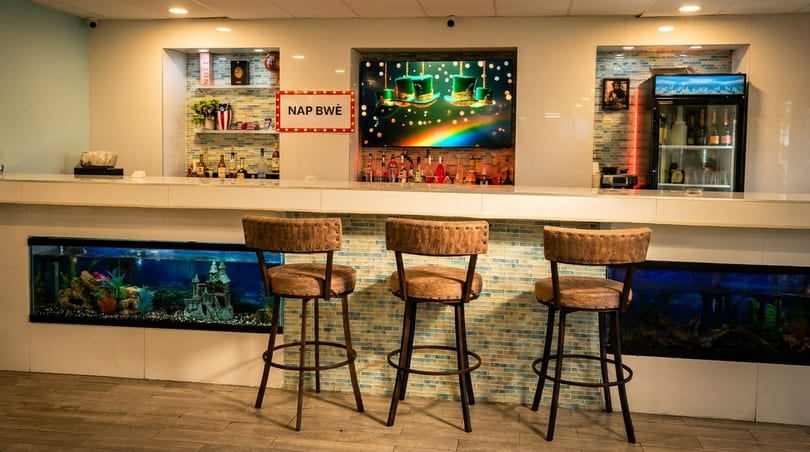 A modern bar area with three stools, an aquarium, and a screen displaying a rainbow.