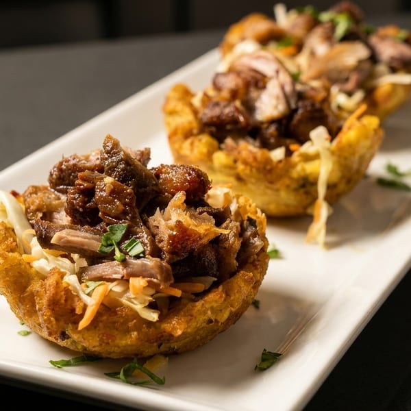 Two golden fried plantain cups filled with savory shredded meat and fresh coleslaw on a white plate.