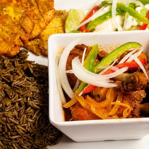 A plate of stewed meat with onions and peppers, dark rice, fried plantains, and a side salad.